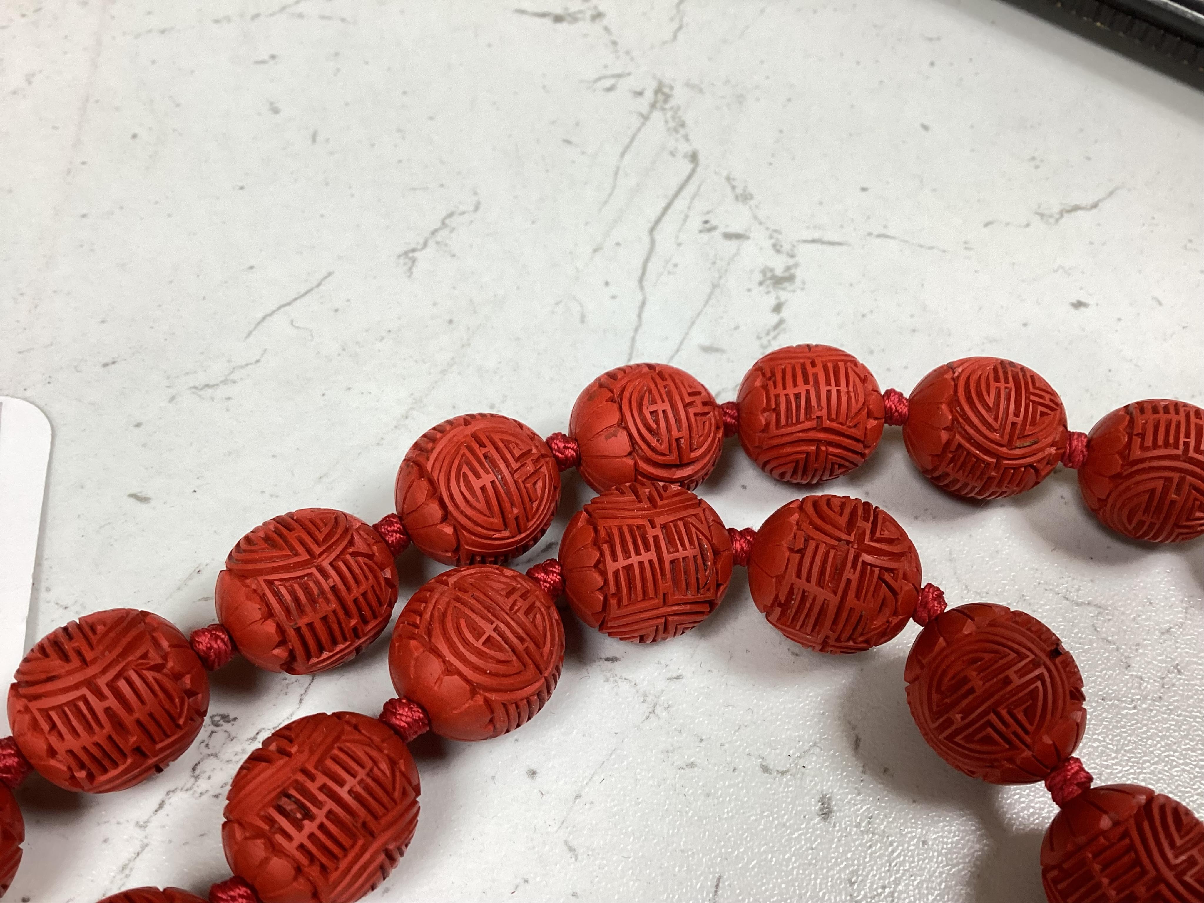 A Chinese red lacquered bead necklace and a bowenite jade figure of a cat